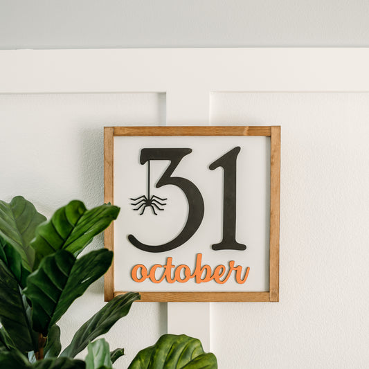 A square-shaped Halloween sign with the date '31 October' written in black, with a spider hanging from the number 1. The sign has a white background and a weathered walnut stain.